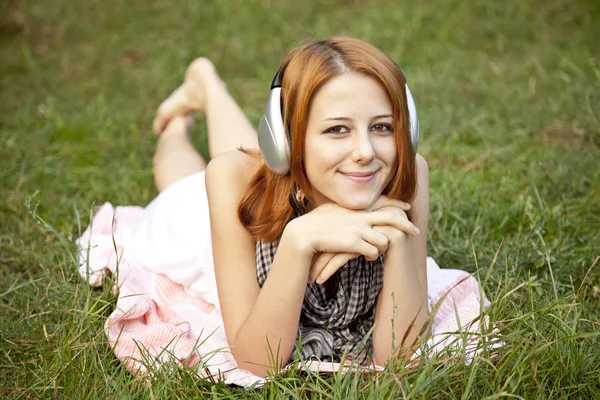 Jonge mode meisje met hoofdtelefoon liggen op groen gras — Stockfoto