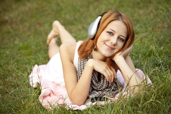 Молодая девушка в наушниках лежит на зеленой траве — стоковое фото