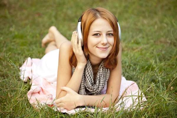 Menina de moda jovem com fone de ouvido deitado na grama verde — Fotografia de Stock