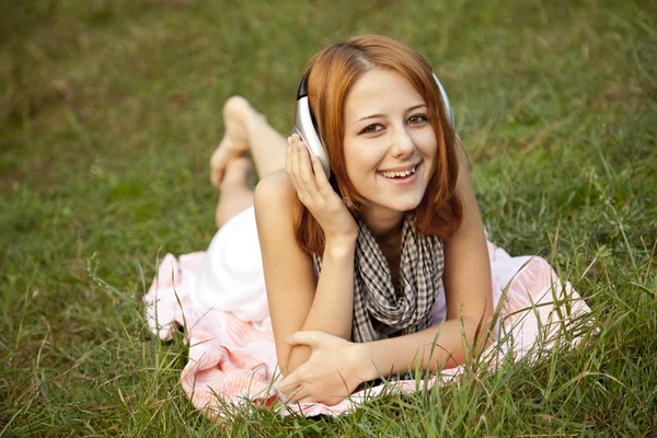 Menina de moda jovem com fone de ouvido deitado na grama verde — Fotografia de Stock