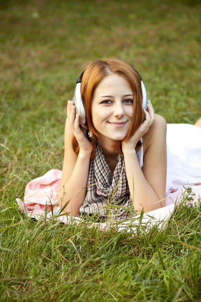 Moda młoda dziewczyna z słuchawek leżącego na zielonej trawie — Zdjęcie stockowe
