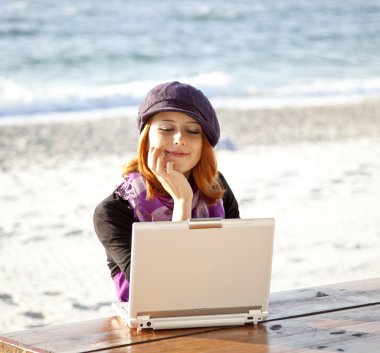 Portrait of red-haired girl with laptop at beach. clipart