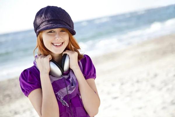 Portret van roodharige meisje met hoofdtelefoon op het strand. — Stockfoto