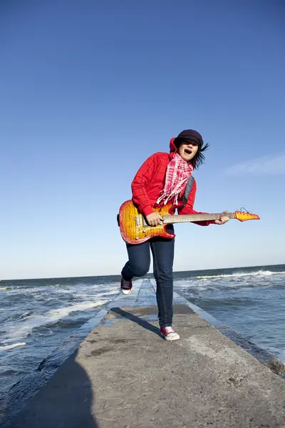 Brunet dívka hrát na kytaru na moři molo v bezvětří den. — Stock fotografie