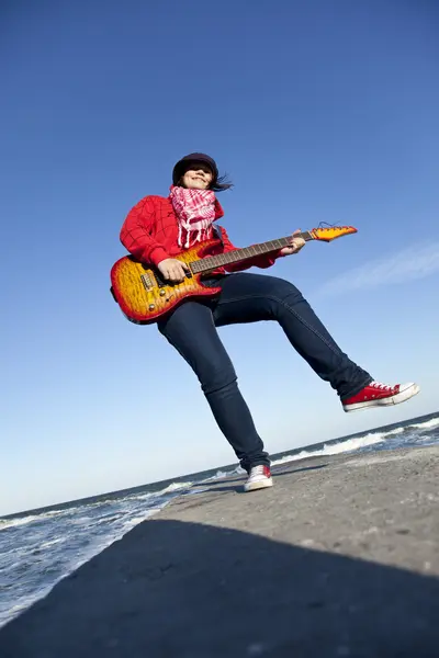 Молодая брюнетка играет на гитаре на морском пирсе в ветреный день . — стоковое фото