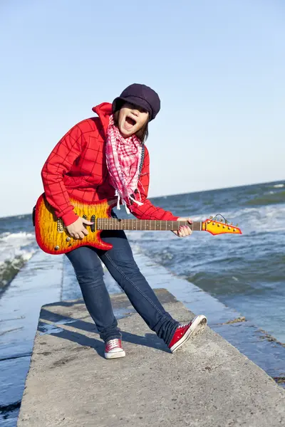 Brunet meisje spelen op gitaar op zee pier in wind dag. — Stockfoto
