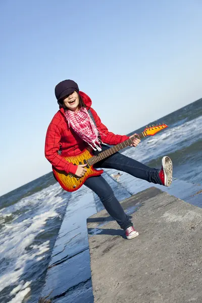 Giovane ragazza bruna suonare la chitarra al molo del mare nel giorno del vento . — Foto Stock