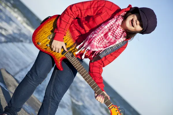 Young brunet girl play on guitar at sea pier in wind day. — Stock Photo, Image