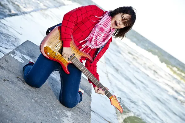 Joven morena chica jugar en la guitarra en el muelle del mar en el día del viento . — Foto de Stock