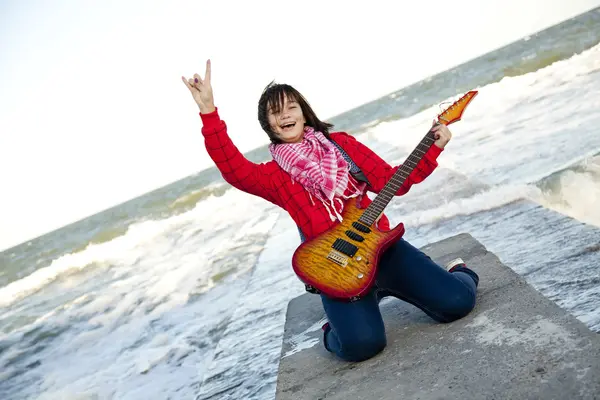 Brunet flicka spela gitarr på havet pier i vind dag. — Stockfoto