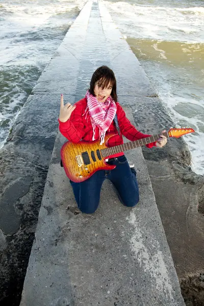 Young brunet girl play on guitar at sea pier in wind day. — Stock Photo, Image