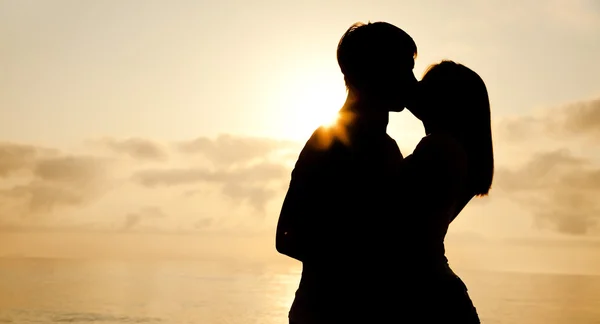 Casal beijando ao nascer do sol na praia . — Fotografia de Stock
