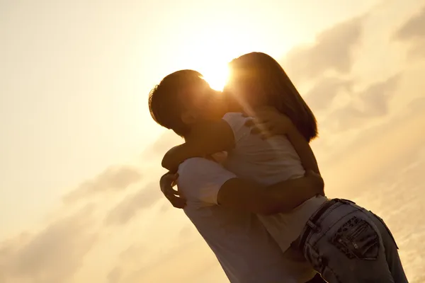 Paar küsst sich im Sonnenaufgang am Strand. — Stockfoto