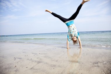 Young girl show an acrobatic on the beach. clipart