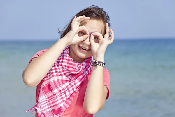 Giovane ragazza bruna sulla spiaggia mostra mano binocolo — Foto Stock