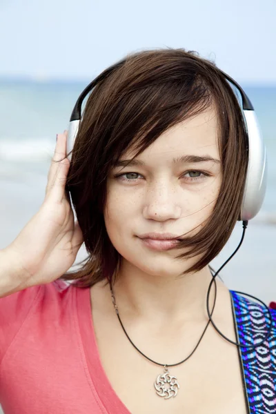 Brunet meisje met hoofdtelefoon en gitaar op het strand. — Stockfoto