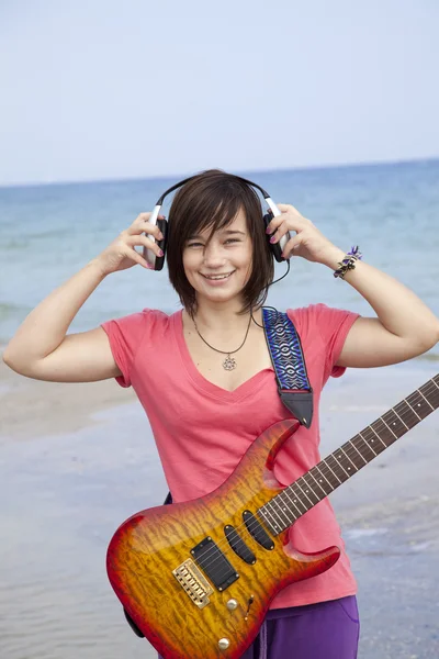 耳机和吉他在海滩上的年轻 brunet 女孩. — 图库照片