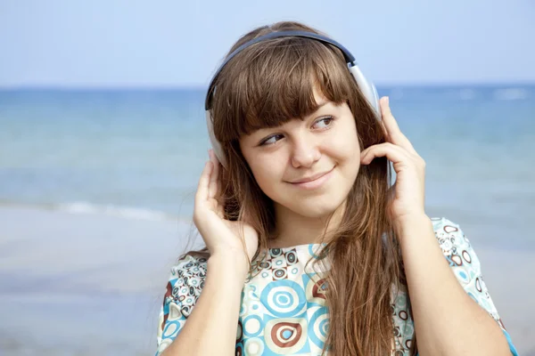 Unga brunhåriga flickan med hörlurar på stranden. — Stockfoto