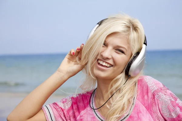 Jonge blonde meisje met hoofdtelefoon op het strand. — Stockfoto
