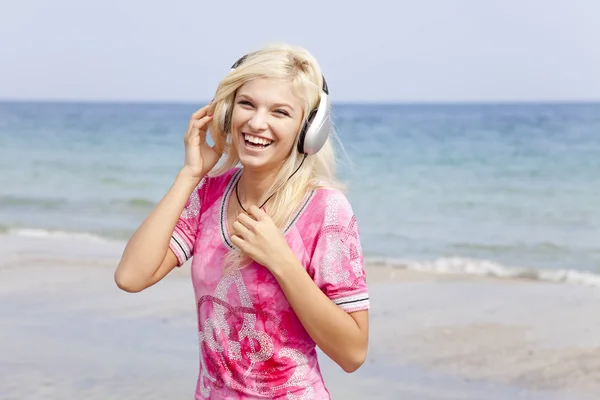 Ung blond tjej med hörlurar på stranden. — Stockfoto