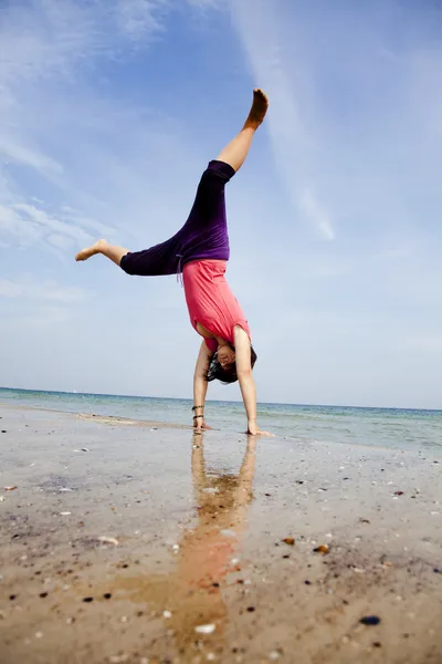 Ung flicka visar en akrobatisk på stranden. — Stockfoto