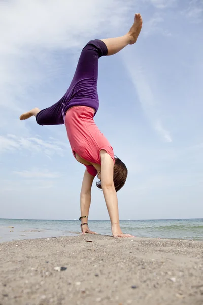 Junges Mädchen zeigt eine Akrobatik am Strand. — Stockfoto