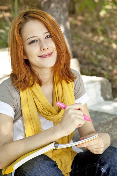 Kızıl saçlı öğrenci kız, açık oturma defter ile. — Stok fotoğraf