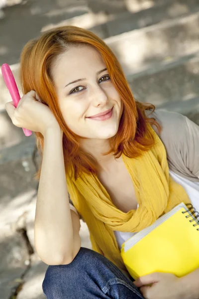 Rödhårig student tjej med anteckningsboken sitter vid utomhus. — Stockfoto