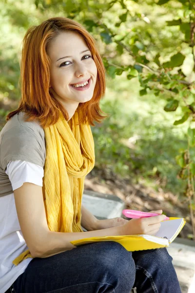 Φοιτητής κοκκινομάλλης κορίτσι με το σημειωματάριο που κάθεται σε εξωτερικούς χώρους. — Φωτογραφία Αρχείου