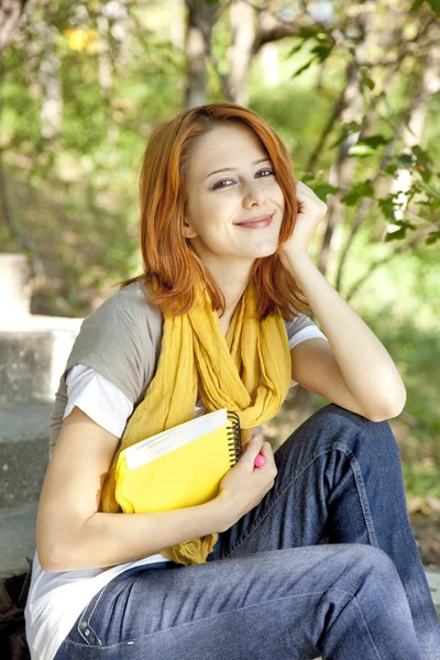 Φοιτητής κοκκινομάλλης κορίτσι με το σημειωματάριο που κάθεται σε εξωτερικούς χώρους. — Φωτογραφία Αρχείου