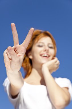 Portrait of red-haired girl in white which show hand V symbol. clipart