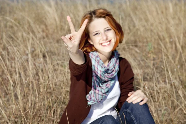 Portrait of red-haired on autumn grass which show hand V symbol. — Stock Photo, Image