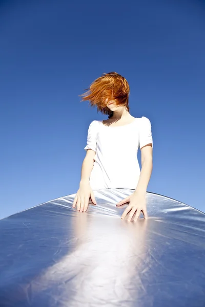 Portrait of red-haired girl in white which keep reflector on blu — Stock Photo, Image