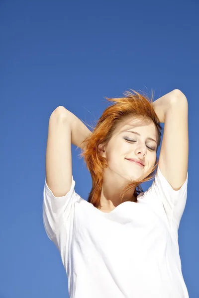 Portrait of red-haired girl in white on blue sky background. — Stock Photo, Image