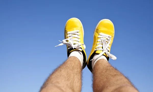 两个脚在蓝蓝的天空背景上的黄色运动鞋. — 图库照片