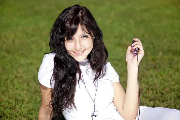 Krásná mladá brunetka poslech hudby na zelené trávě v — Stock fotografie