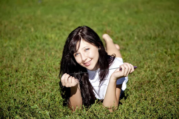 Bella ragazza bruna ascoltare musica su erba verde nel — Foto Stock
