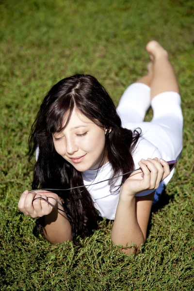 Bella ragazza bruna ascoltare musica su erba verde nel — Foto Stock