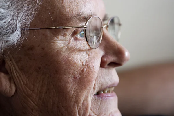 Elderly woman gazing and smiling from si — Stock Photo, Image