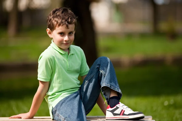 Ładny mały chłopiec siedzi na ławce — Zdjęcie stockowe