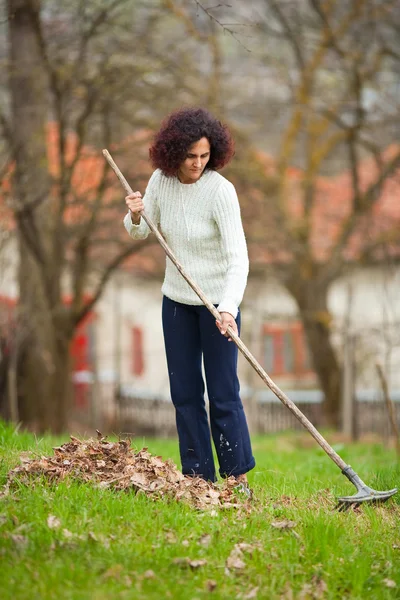 Rossa donna utilizzando un rastrello per la pulizia — Foto Stock