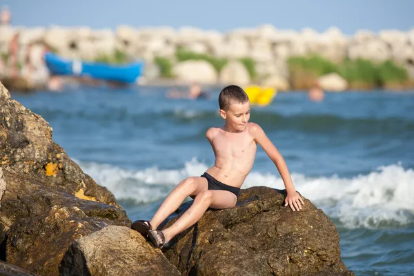 Kleine jongen zittend op de rotsen op zee — Stockfoto