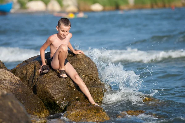 Kleine jongen zittend op de rotsen op zee — Stockfoto