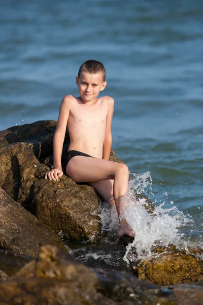 Маленький мальчик, сидящий на скалах в море — стоковое фото