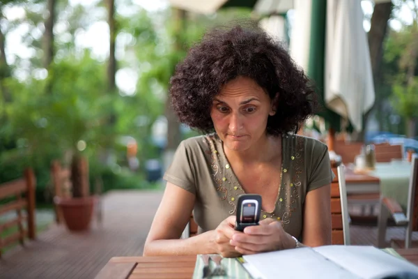 Ung kvinna med hjälp av mobiltelefon i en restaurang — Stockfoto