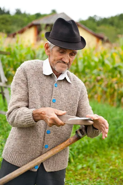 Старик, использующий косу — стоковое фото