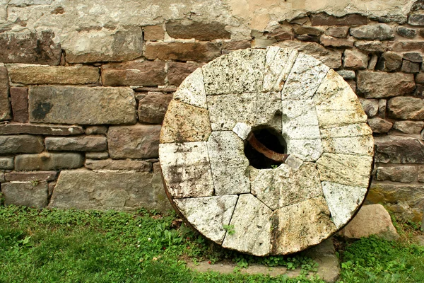 Starý mlýnský kámen, opíraje se o zeď — Stock fotografie