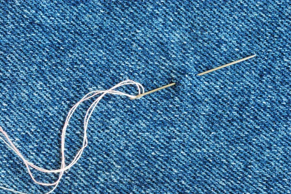 Die Nadel mit einem Faden durch die Jeans — Stockfoto