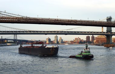 A tugboat pulls a container ship passed the Brooklyn Bridge clipart