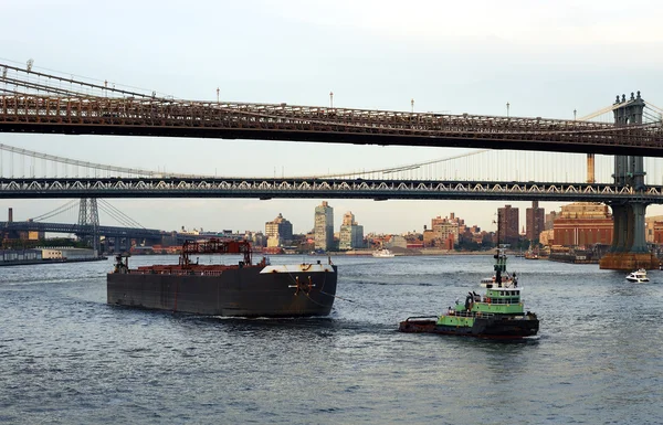 A tugboat pulls a container ship passed the Brooklyn Bridge — Stock Photo, Image
